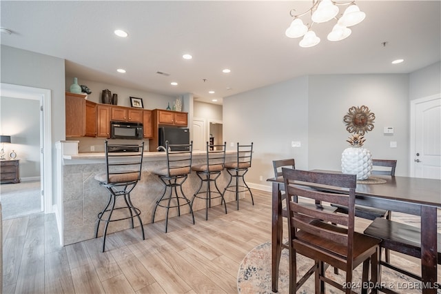 kitchen featuring hanging light fixtures, fridge, a kitchen bar, and light wood-type flooring