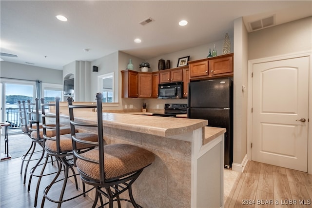 kitchen featuring a breakfast bar, black appliances, kitchen peninsula, and light wood-type flooring