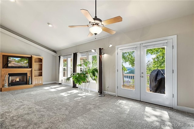 unfurnished living room featuring carpet floors, baseboards, vaulted ceiling, a lit fireplace, and french doors