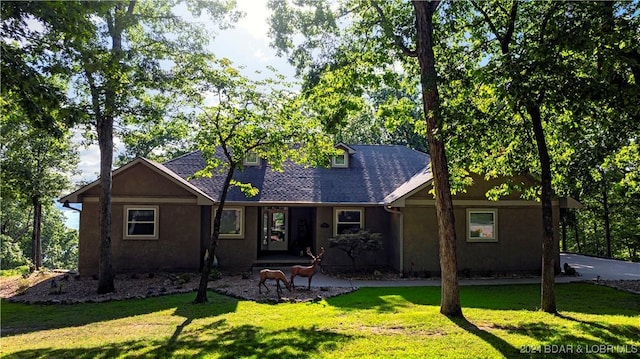 view of front of home with a shingled roof, a front yard, and stucco siding