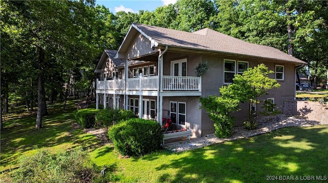 back of property with a lawn, a balcony, and stucco siding