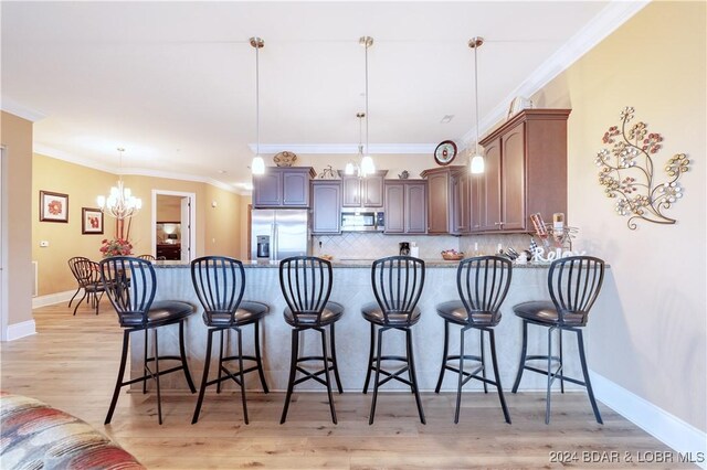 kitchen featuring light hardwood / wood-style flooring, tasteful backsplash, hanging light fixtures, ornamental molding, and stainless steel appliances