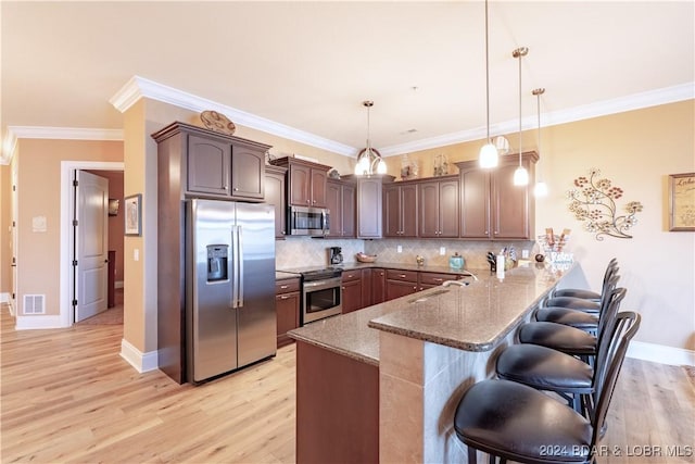 kitchen with appliances with stainless steel finishes, decorative backsplash, light wood-type flooring, stone countertops, and hanging light fixtures