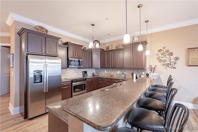 kitchen featuring kitchen peninsula, decorative light fixtures, sink, appliances with stainless steel finishes, and a kitchen bar