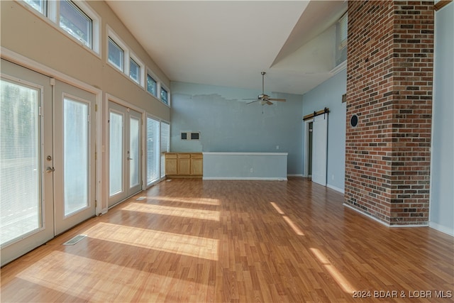 interior space with a barn door, french doors, high vaulted ceiling, and light wood-type flooring