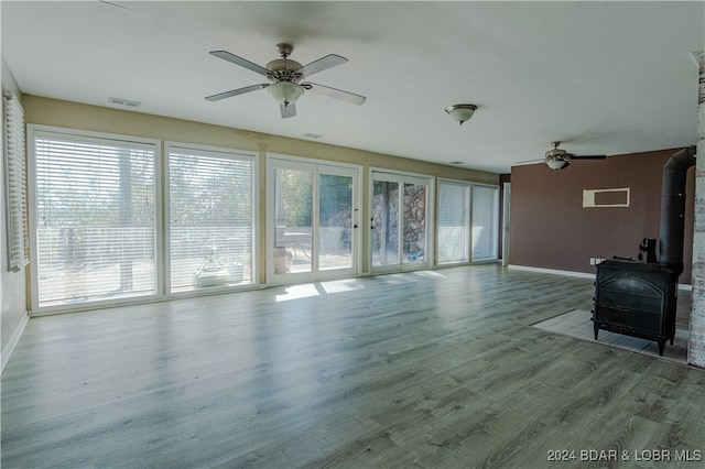 unfurnished living room featuring a wood stove, ceiling fan, hardwood / wood-style floors, and a healthy amount of sunlight