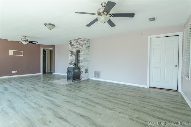 unfurnished living room featuring a wood stove, ceiling fan, and light hardwood / wood-style flooring