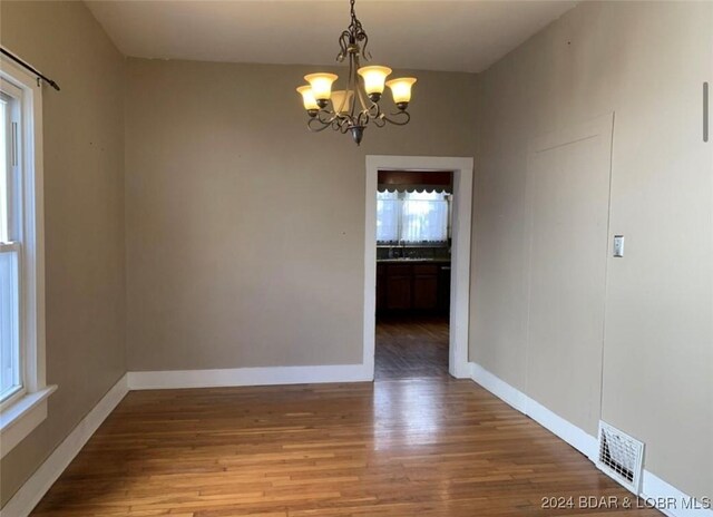 empty room featuring sink, an inviting chandelier, hardwood / wood-style floors, and a healthy amount of sunlight