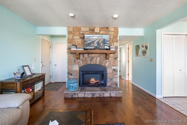 living room with hardwood / wood-style flooring, a textured ceiling, and a stone fireplace