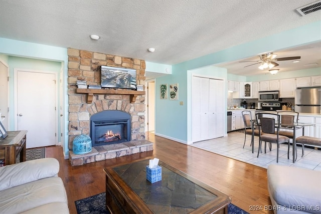 living room with ceiling fan, a fireplace, a textured ceiling, and light hardwood / wood-style floors