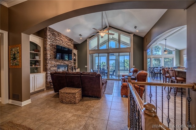 interior space featuring ceiling fan, built in shelves, high vaulted ceiling, and a stone fireplace