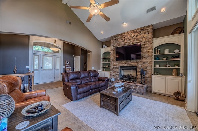 tiled living room featuring ceiling fan, built in shelves, high vaulted ceiling, and a stone fireplace