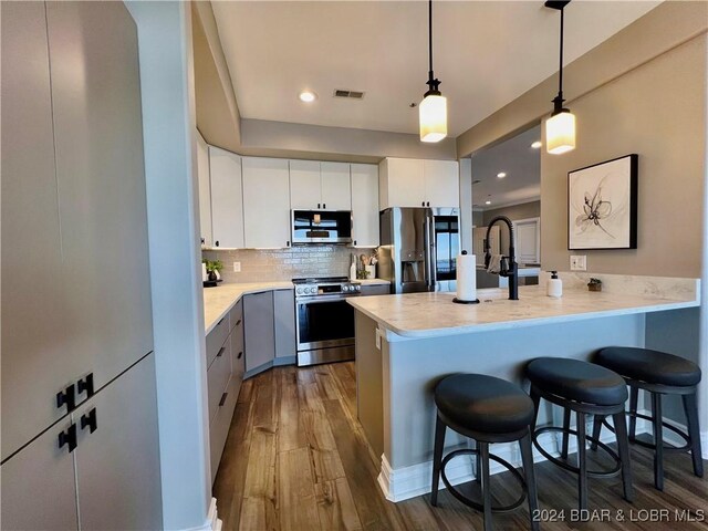 kitchen with backsplash, wood-type flooring, white cabinetry, kitchen peninsula, and stainless steel appliances