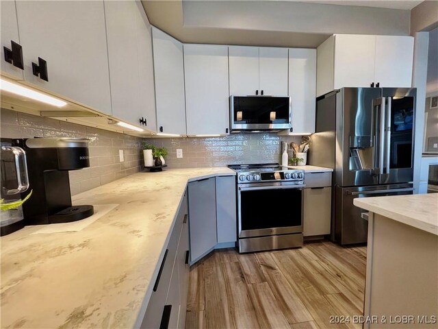 kitchen with tasteful backsplash, white cabinetry, appliances with stainless steel finishes, light stone countertops, and light hardwood / wood-style floors