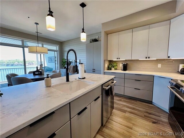 kitchen featuring light wood-type flooring, backsplash, pendant lighting, appliances with stainless steel finishes, and sink