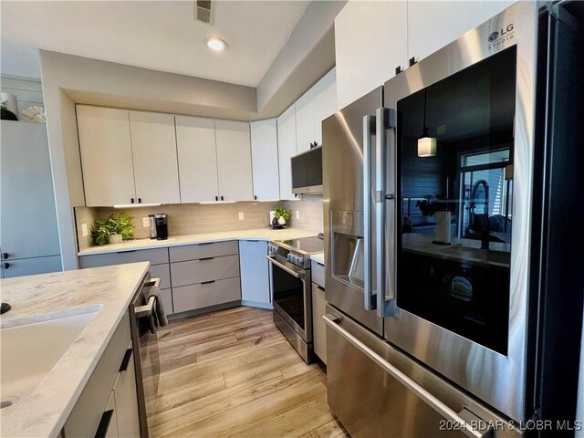 kitchen featuring light hardwood / wood-style flooring, decorative backsplash, stainless steel appliances, pendant lighting, and white cabinets