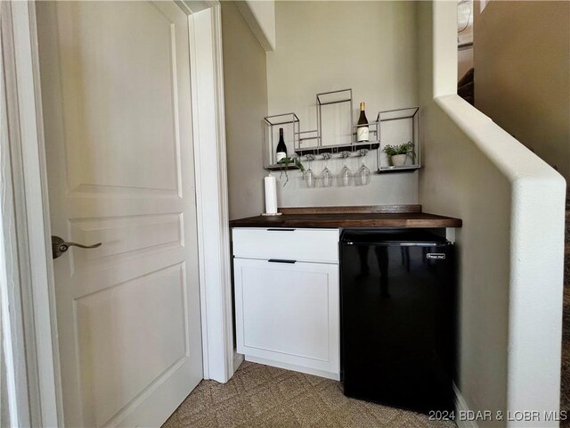 bar with butcher block counters, fridge, white cabinetry, and light colored carpet