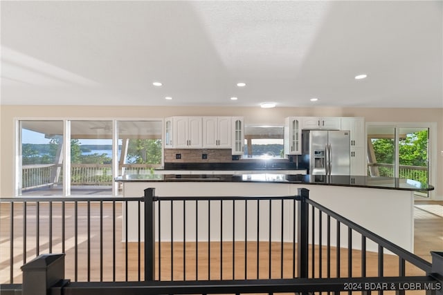 kitchen with white cabinetry, stainless steel refrigerator with ice dispenser, a healthy amount of sunlight, and tasteful backsplash