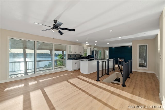 kitchen with light wood-type flooring, a kitchen island, white cabinets, a water view, and stainless steel refrigerator with ice dispenser