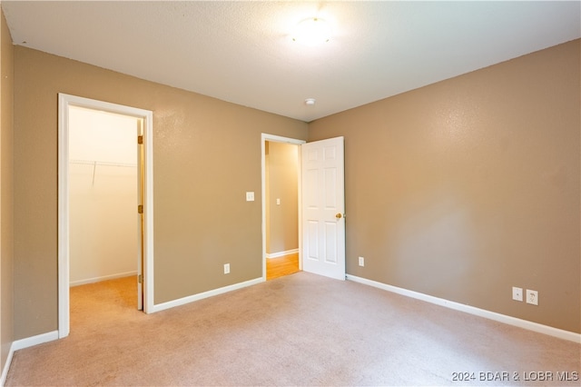 unfurnished bedroom with a spacious closet, light carpet, and a closet