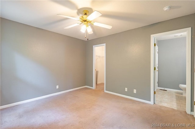 unfurnished bedroom with a closet, a spacious closet, ensuite bathroom, ceiling fan, and light carpet