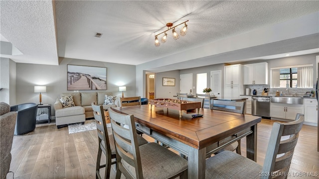 dining room with sink, a textured ceiling, and light hardwood / wood-style flooring