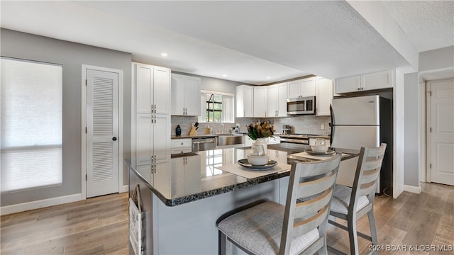 kitchen with light hardwood / wood-style flooring, a kitchen island, white cabinetry, a breakfast bar area, and stainless steel appliances