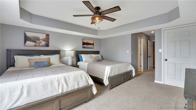 carpeted bedroom with ceiling fan and a raised ceiling