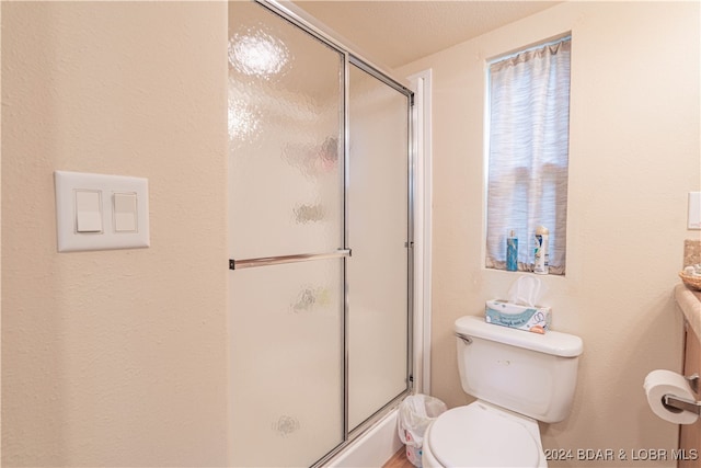 bathroom with toilet, a textured ceiling, and a shower with shower door