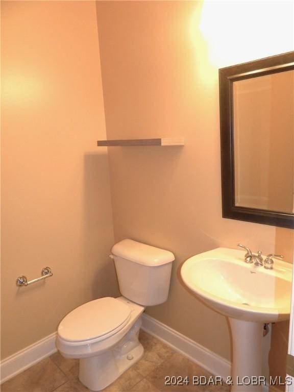 half bath with tile patterned flooring, toilet, and baseboards