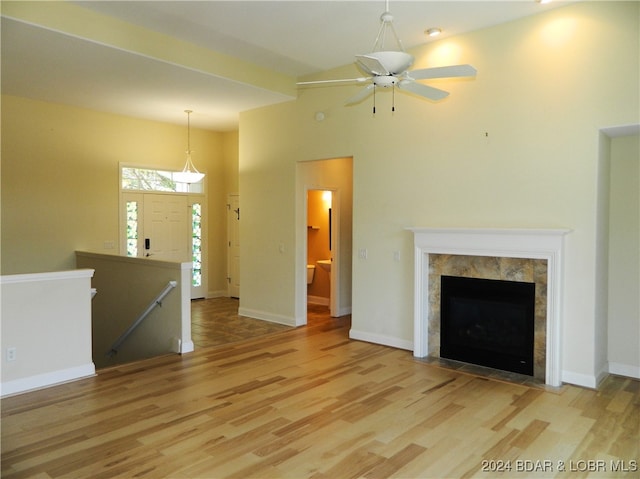 unfurnished living room with ceiling fan, a high ceiling, light hardwood / wood-style flooring, and a tile fireplace