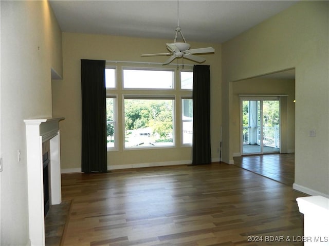 unfurnished living room featuring dark wood-type flooring, a fireplace, baseboards, and ceiling fan