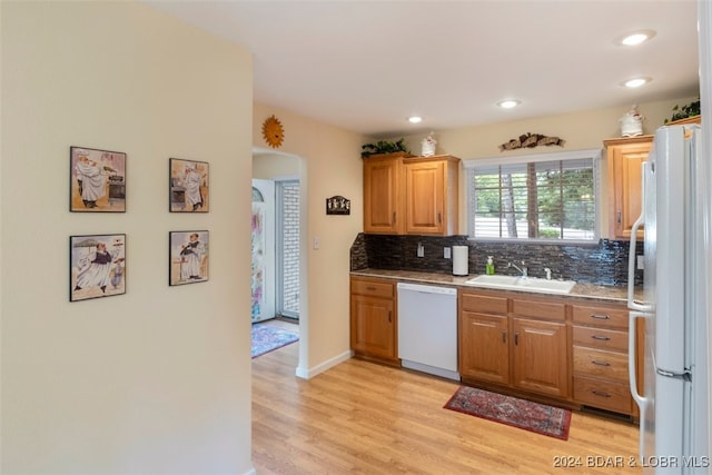 kitchen with white appliances, light hardwood / wood-style flooring, sink, decorative backsplash, and stone counters