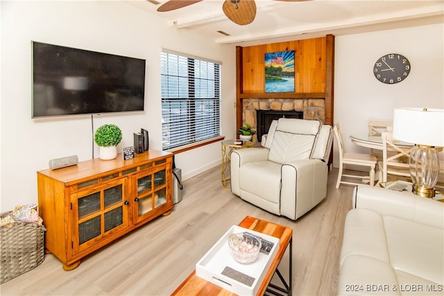 living room featuring light hardwood / wood-style flooring, ceiling fan, beam ceiling, and a fireplace