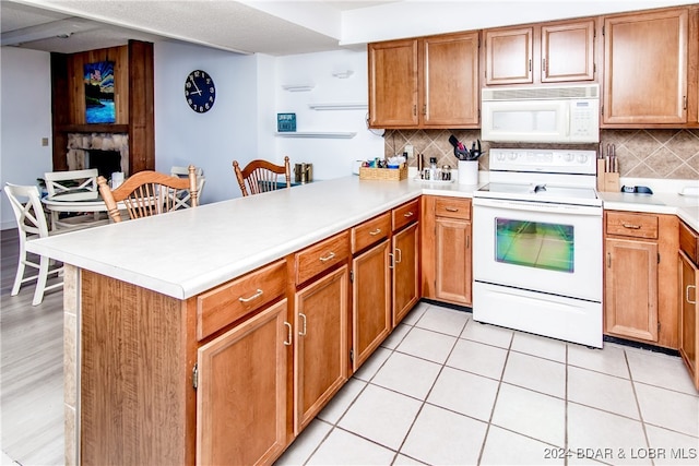 kitchen featuring light tile patterned floors, a fireplace, white appliances, kitchen peninsula, and tasteful backsplash