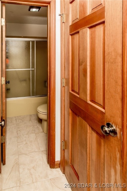 bathroom featuring toilet, tile patterned floors, and enclosed tub / shower combo