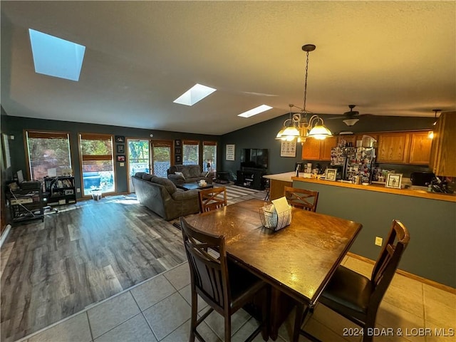 tiled dining area with lofted ceiling with skylight and ceiling fan with notable chandelier