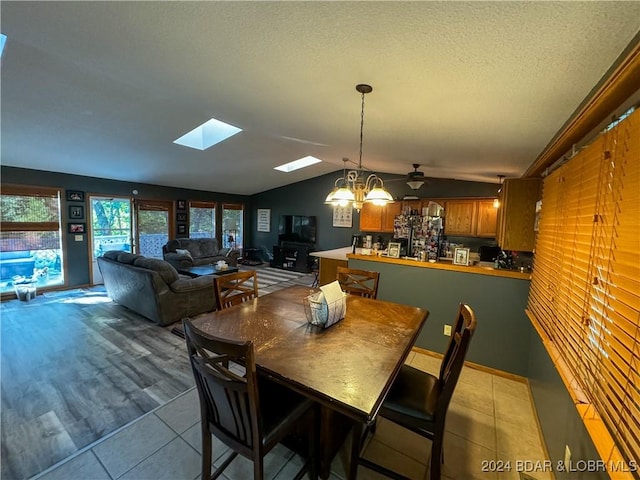 tiled dining space with ceiling fan and lofted ceiling with skylight