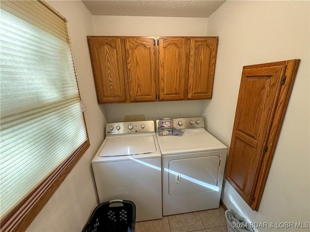 laundry area with a textured ceiling, a wealth of natural light, washing machine and dryer, cabinets, and light tile patterned floors