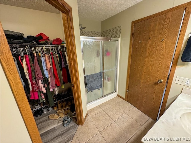 bathroom with a textured ceiling, a shower with door, vanity, and tile patterned flooring