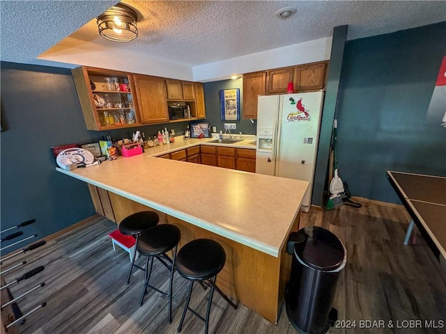 kitchen with a breakfast bar, kitchen peninsula, wood-type flooring, sink, and white refrigerator with ice dispenser