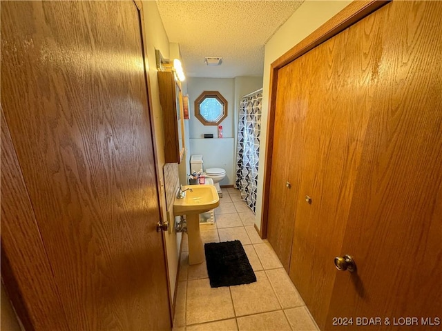 bathroom featuring toilet, tile patterned floors, a textured ceiling, and curtained shower