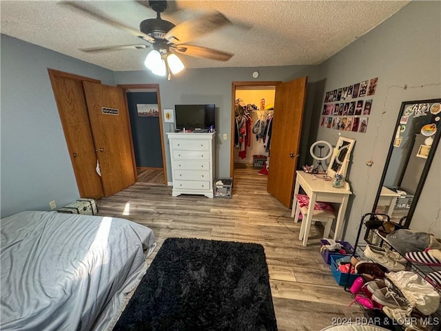 bedroom with a spacious closet, ceiling fan, light wood-type flooring, a closet, and a textured ceiling