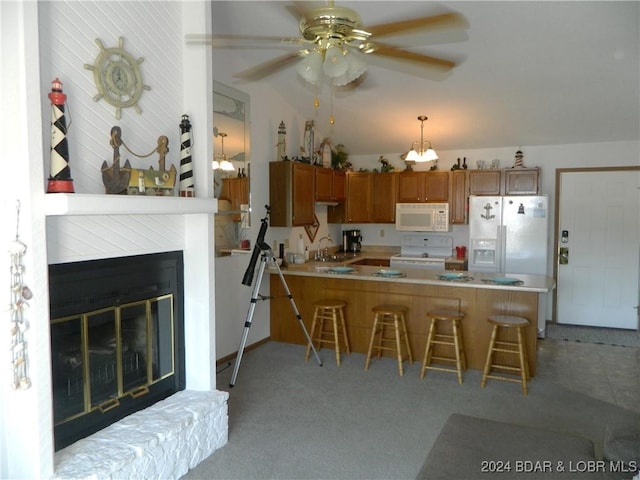 kitchen with a breakfast bar, a sink, a glass covered fireplace, white appliances, and a peninsula