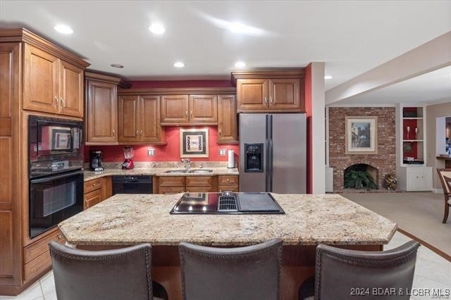 kitchen with a breakfast bar, black appliances, a large fireplace, and light stone counters