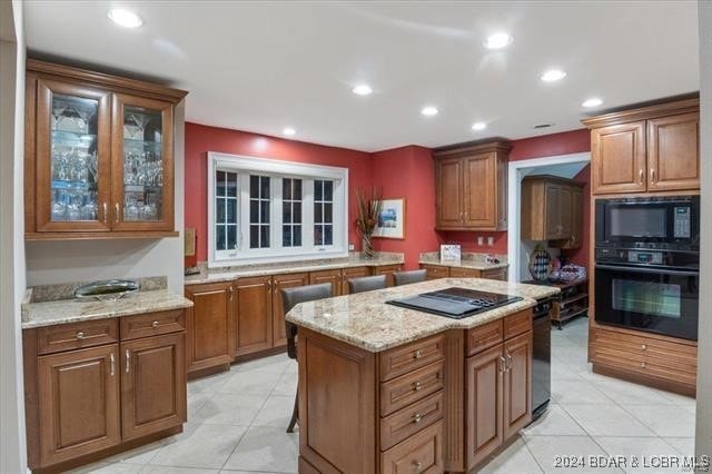 kitchen with a kitchen island, light stone counters, light tile patterned floors, and black appliances