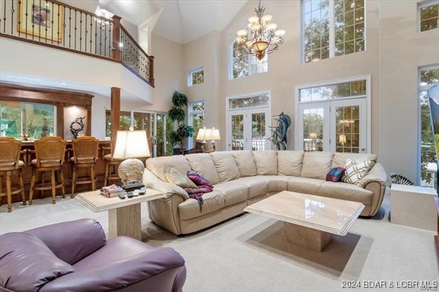 living room with a towering ceiling, an inviting chandelier, carpet floors, and french doors