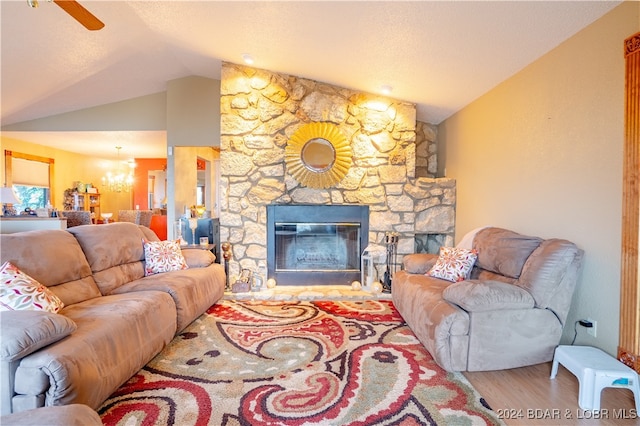 living room featuring ceiling fan with notable chandelier, a stone fireplace, vaulted ceiling, and hardwood / wood-style flooring