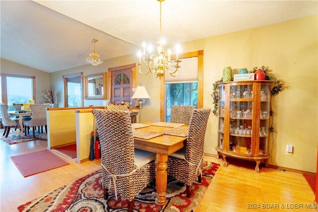 dining space featuring hardwood / wood-style floors, vaulted ceiling, an inviting chandelier, and a wealth of natural light