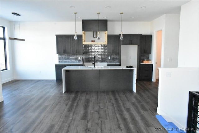 kitchen featuring dark hardwood / wood-style floors, decorative light fixtures, tasteful backsplash, and an island with sink